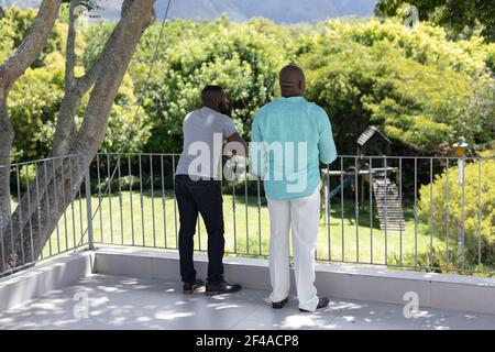 Padre e figlio adulto afro-americano senior in piedi sulla terrazza in giardino soleggiato Foto Stock