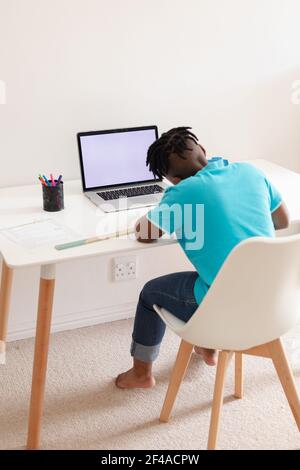 Vista posteriore del ragazzo afroamericano seduto alla scrivania con il computer portatile che lavora a scuola Foto Stock