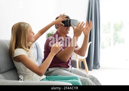Nipote caucasica seduta sul divano accanto al nonno che regola la sua vr cuffia Foto Stock