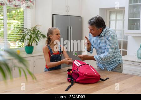 Nonno caucasico che dà nipotina pranzo al sacco e lollipop in cucina Foto Stock