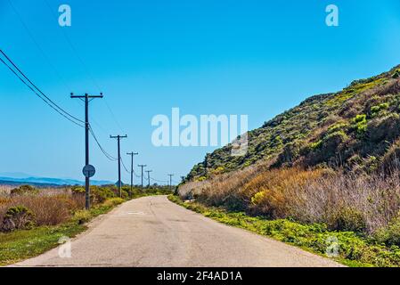 Il pavimento si curva intorno alla collina fiancheggiata da pali telefonici sotto il cielo blu. Foto Stock