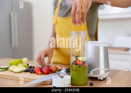 Donna di razza mista che fa una bevanda sana e sorridente dentro una cucina Foto Stock