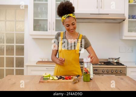 Donna di razza mista che fa una bevanda sana e sorridente dentro una cucina Foto Stock