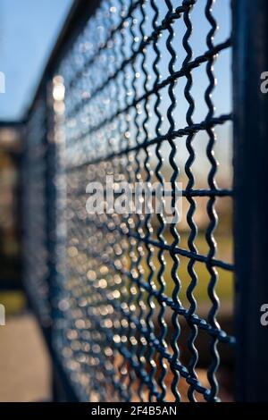 Struttura railing astratta con bokeh e luci dapples. Vista prospettica sfocata del recinto blu in metallo con sfondo blu e verde. Foto Stock