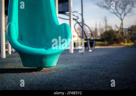 Scivolo parziale nel parco giochi, mattina presto in una giornata di sole. Vetrino blu brillante con superficie in gomma blu scuro assorbente gli urti. Messa a fuoco selettiva Foto Stock