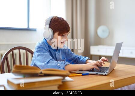 Sorridente allievo in cuffia durante una lezione online di fronte a un monitor portatile. Scrive un messaggio in linea all'insegnante. Conc. Apprendimento online Foto Stock