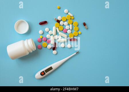 Compresse, pillole, capsule e termometro digitale multicolore su sfondo blu. Concetto di trattamento per una persona malata. Vista dall'alto Foto Stock