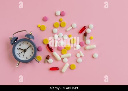 Molte pillole diverse con sveglia su sfondo rosa. Tempo di prendere il farmaco. Vista dall'alto Foto Stock