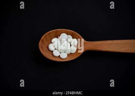 Pillole bianche, in un cucchiaio di legno su sfondo nero. Medicina e concetto di salute. Prodotti farmaceutici. Vista dall'alto. Compresse e vitamine. Foto Stock