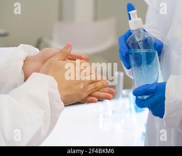 Ricercatori epidemiologici in abbigliamento protettivo anti-virus lavando le mani con gel di alcool prima di iniziare l'esperimento in un laboratorio scientifico. HY Foto Stock