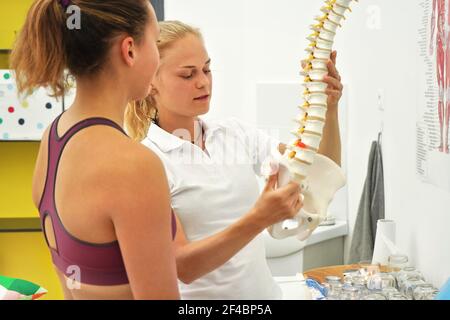 Paziente giovane donna alla consultazione di fisioterapia, terapista che spiega le sue ossa posteriori sul modello della spina dorsale Foto Stock