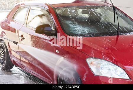 Auto rossa lavata in autolavaggio, spruzzatura d'acqua sulle ruote laterali e anteriori Foto Stock