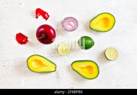 Metà avocado, lime e cipolle - ingredienti base guacamole su tavola da lavoro bianca, foto piatta Foto Stock