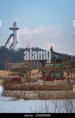 PyeongChang, Corea del Sud - 12 Febbraio 2018: Padiglione Cheongsong sull'isola di Pine a Pyeongchang, Corea del Sud con sci olimpico che salta sulla collina sul retro Foto Stock