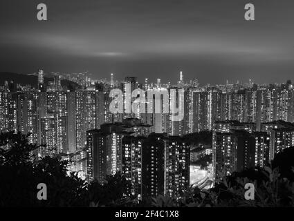 Vista notturna di appartamenti residenziali blocchi Kowloon, Hong Kong in bianco e nero. Le nuvole sono illuminate da edifici luminosi. Foto Stock