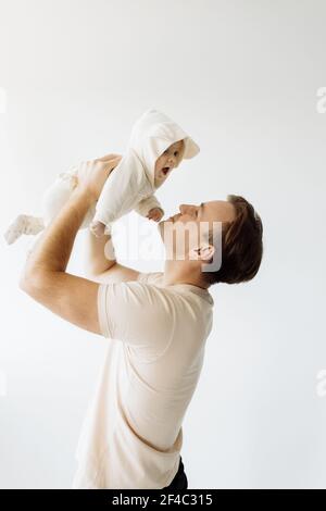 Papà felice tiene il bambino tra le braccia, sollevandolo. La adorabile piccola figlia è molto contentissima. Gioca insieme in una stanza su sfondo bianco. Famiglia Foto Stock