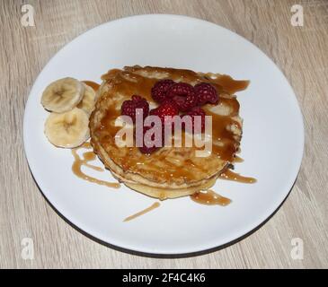 I gustosi pancake con sciroppo di caramello, lamponi e alcune fette di banana serviti su un piatto bianco Foto Stock