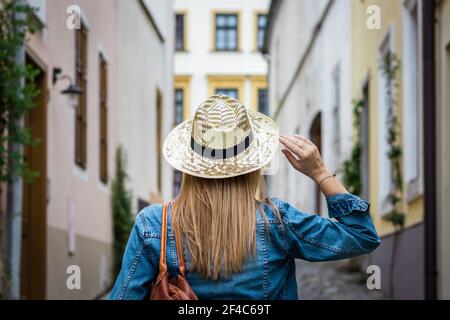 Donna bionda con giacca in denim e cappello di paglia. Donna turistica a piedi nelle strade della città Foto Stock