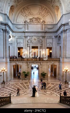 Una sposa e uno sposo posano per scattare foto sulla grande scala nella rotonda di San Francisco, il Municipio della California. Foto Stock