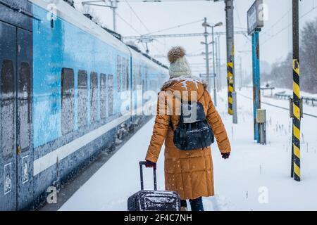 La donna con i bagagli è a bordo per allenarsi sulla stazione ferroviaria durante la nevica Foto Stock