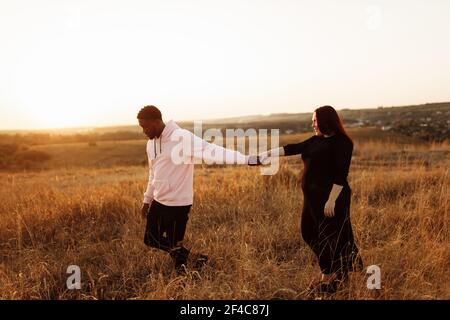 Bella coppia a piedi al campo, attraente marito che tiene le mani adorabile moglie, donna sorrise, felice famiglia trascorrere il tempo insieme Foto Stock