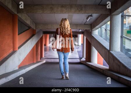 Giovane donna alla moda che cammina nel parcheggio pubblico. Elegante donna bionda con giacca corduroy e jeans. Foto Stock