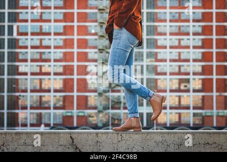 Donna che indossa pantaloni in denim e scarpe eleganti in pelle in città. Architettura moderna come sfondo. Concetto di bellezza e moda Foto Stock