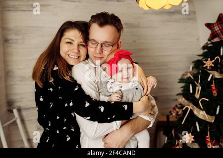 Ritratto di genitori felici con bella bambina vicino albero di Natale, bel padre tenere la bambina in armi, la madre sorrise, giovane Foto Stock