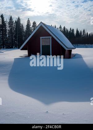 Haparanda / Svezia - 13 MARZO 2021: Un piccolo capannone che getta un'ombra sulla neve bianca pura in una giornata di sole in inverno. Foto Stock
