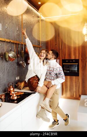 Bella coppia coccolarsi in cucina a casa, sorridendo, godere di momenti teneri, cucina xmas cena, prepararsi alla festa di Natale, accogliente inverno Foto Stock