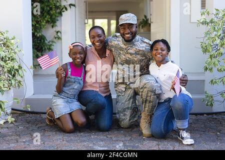 Sorridente padre soldato afroamericano abbracciando moglie e bambini fronte della casa Foto Stock