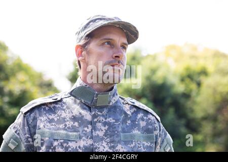 Soldato maschio caucasico indossando camo affaticati e cappellino in piedi all'aperto guardando via Foto Stock
