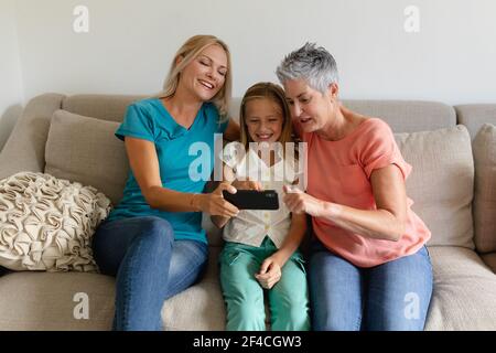 Madre caucasica seduta sul divano guardando lo smartphone sorridendo figlia e nonna Foto Stock