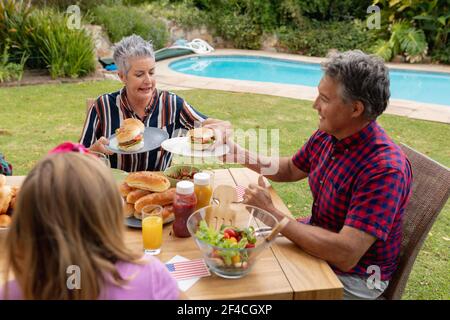 Sorridente uomo caucasico anziano che serve la famiglia prima di mangiare insieme in giardino Foto Stock