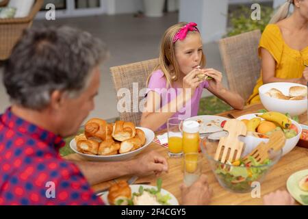 Caucasica ragazza mangiare hamburger seduta a tavola con la famiglia avendo pasto in giardino Foto Stock