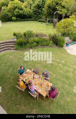 Vista ad alto angolo della famiglia caucasica di tre generazioni seduta a. pasto al tavolo in giardino Foto Stock