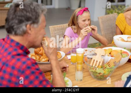 Caucasica ragazza e nonno mangiare hamburger a tavola con la famiglia pasto in giardino Foto Stock