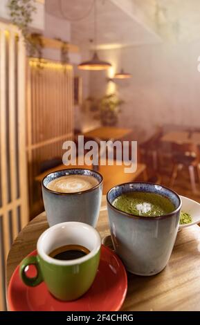 Tazze di caffè, caffè espresso e latte matcha sul tavolo in un caffè sfondo sfocato Foto Stock