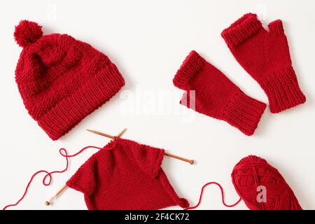Progetto di Unione in corso. Cappello invernale e guanti lavorati a maglia con filo rosso su sfondo bianco. Foto Stock