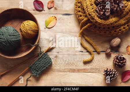 Un pezzo di maglia con aghi di legno e filo tra foglie e coni di pino, lavorazione autunnale. Foto Stock