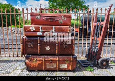 Valigie in vecchio cuoio e carrello di Porter sulla piattaforma della stazione sulla Severn Valley Railway, Worcestershire, Inghilterra Foto Stock