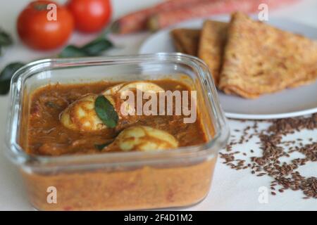 Curry bollito all'uovo, un sugo a base di pomodoro di anacardi servito con pane piatto indiano integrale di grano fatto di carote grattugiate e semi di lino in polvere. Scatto su w Foto Stock