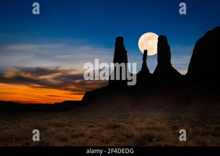 Luna che sorge dietro una silhouette di Three Sisters, Monument Valley, Arizona, USA Foto Stock