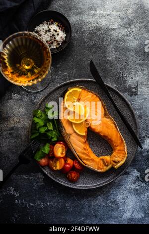 Bistecca di salmone alla griglia con pomodori, limone e un bicchiere di vino bianco Foto Stock