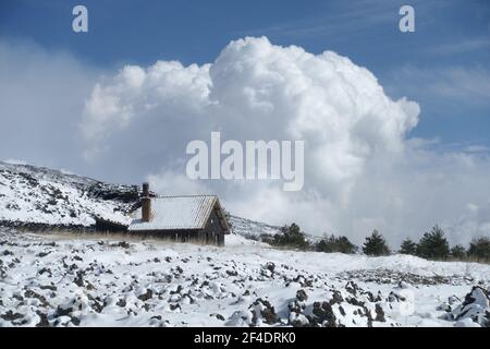 rifugio in pietra di montagna innevato in Sicilia sullo sfondo A. Grandi nuvole bianche nel cielo blu del Parco dell'Etna Foto Stock