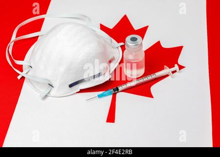 Flag Canada, maschera facciale N95, siringa con ago e flaconcino. Concetto di distribuzione del vaccino del coronavirus Covid-19, carenza di approvvigionamento e crisi sanitaria Foto Stock