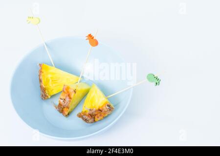 Spiedini di ananas sbucciati e tagliati a triangoli con bastoncini decorati all'interno di una ciotola blu con sfondo bianco Foto Stock