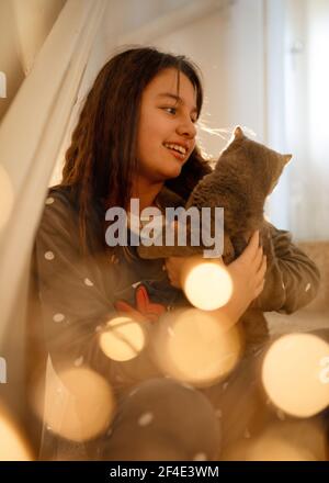 Ragazze in pigiama grigio abbracciano un gatto blu seduto sopra a sulle scale Foto Stock