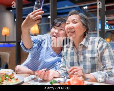 Madre e figlia felici che prendono selfie durante un pasto dentro ristorante Foto Stock