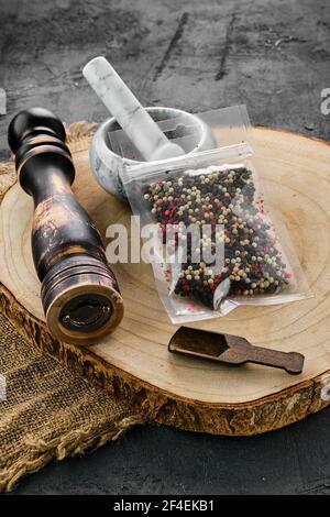 Sezione trasversale di legno con miscela di peperoni in confezione di plastica e mortaio di pietra e mulino Foto Stock